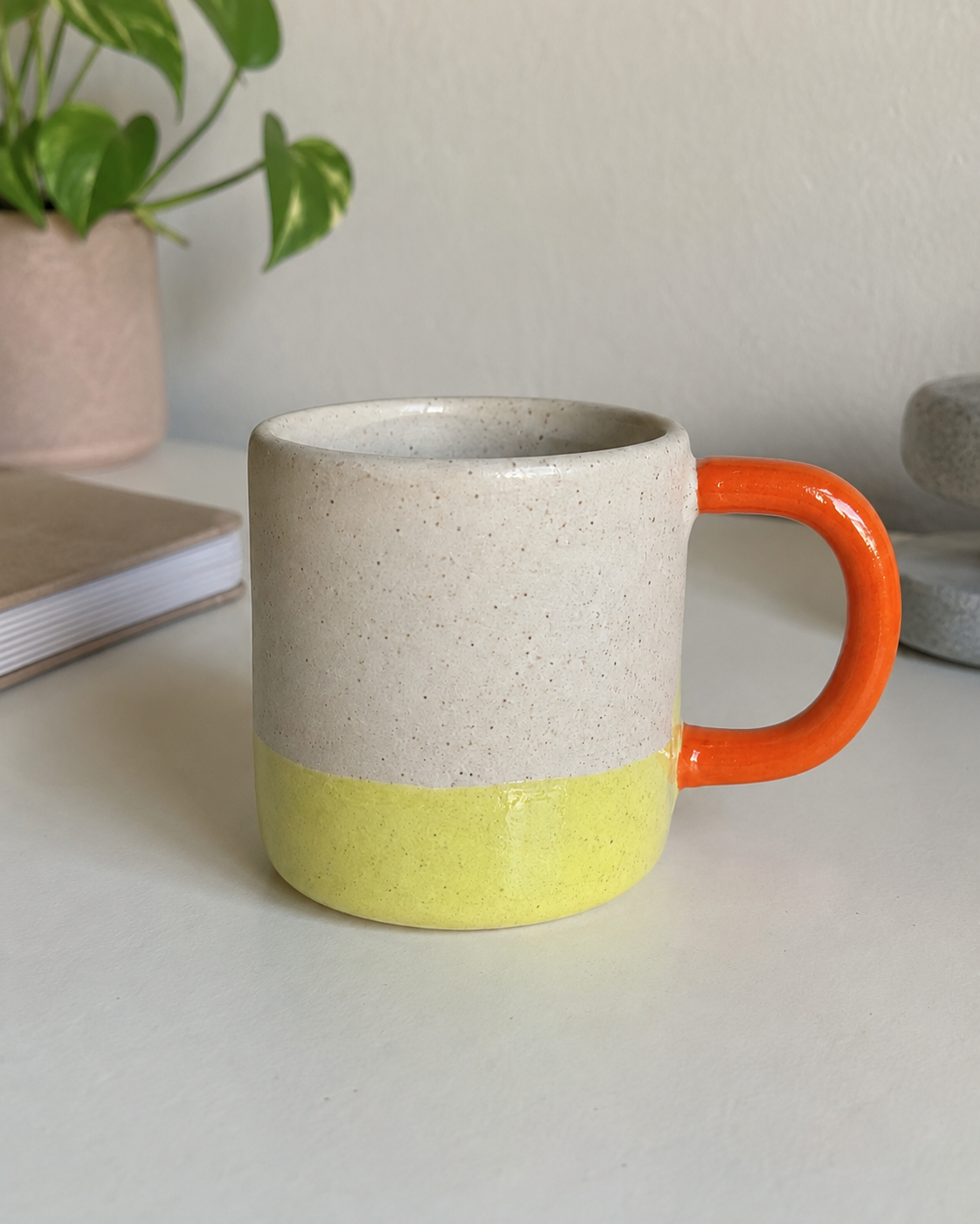 Original photo of a speckled ceramic mug with a citron glaze dip and orange handle